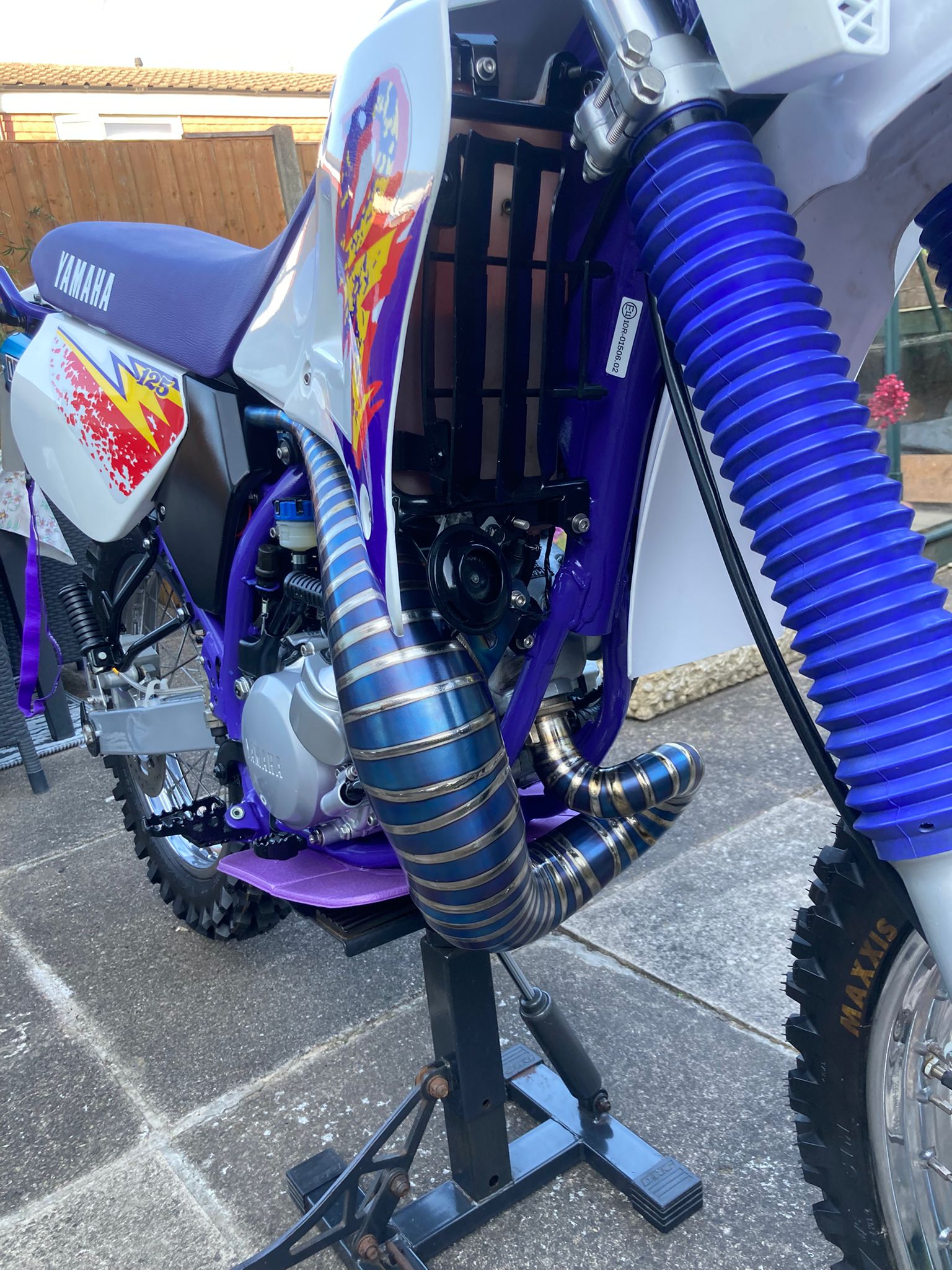 Yamaha dirt bike with custom exhaust pipes on a stand outdoors.