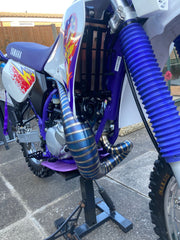 Yamaha dirt bike with custom exhaust pipes on a stand outdoors.