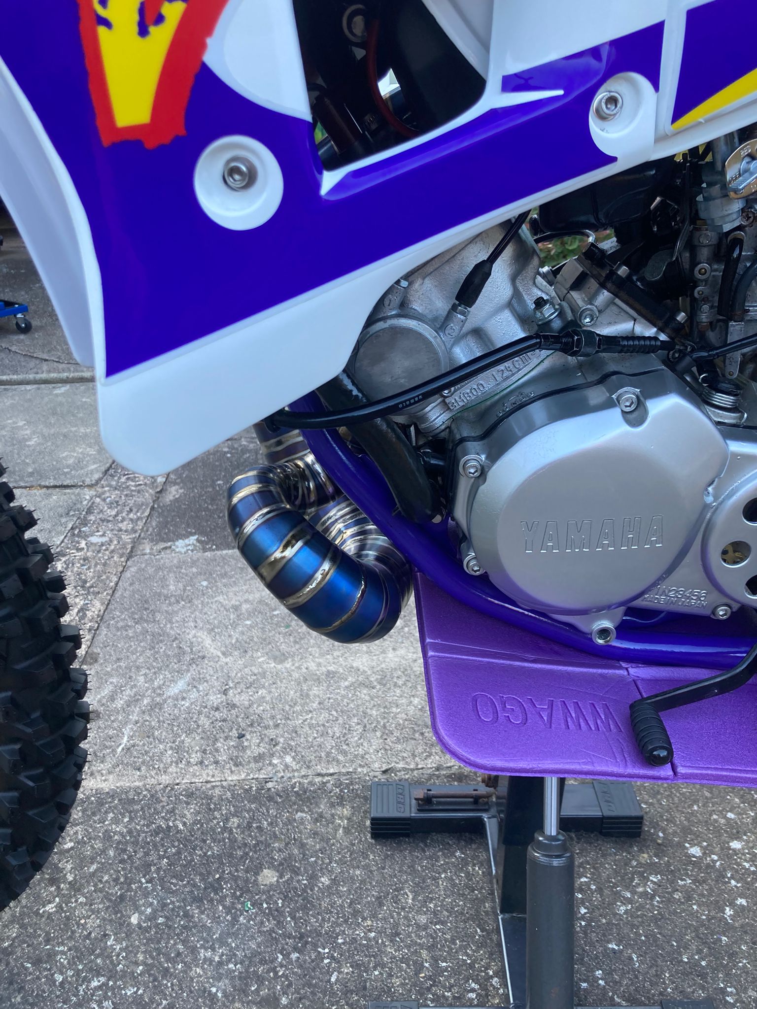 Close-up of a purple and white dirt bike with visible branding on a concrete surface.